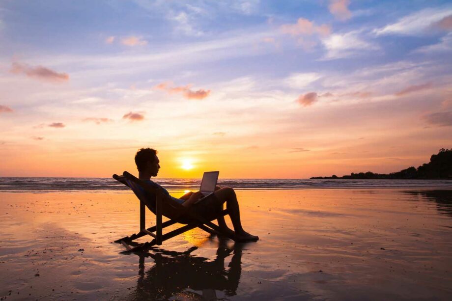 Man working on laptop from the beach at sunset using TGX Remote Desktop software